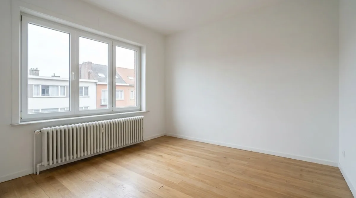 Séjour vide aux murs blancs, parquet en chêne, radiateur sous une porte-fenêtre